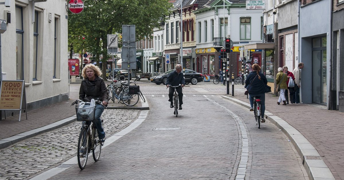 Fietsers rijden door een Nederlandse winkelstraat met klinkers en winkels aan weerszijden.